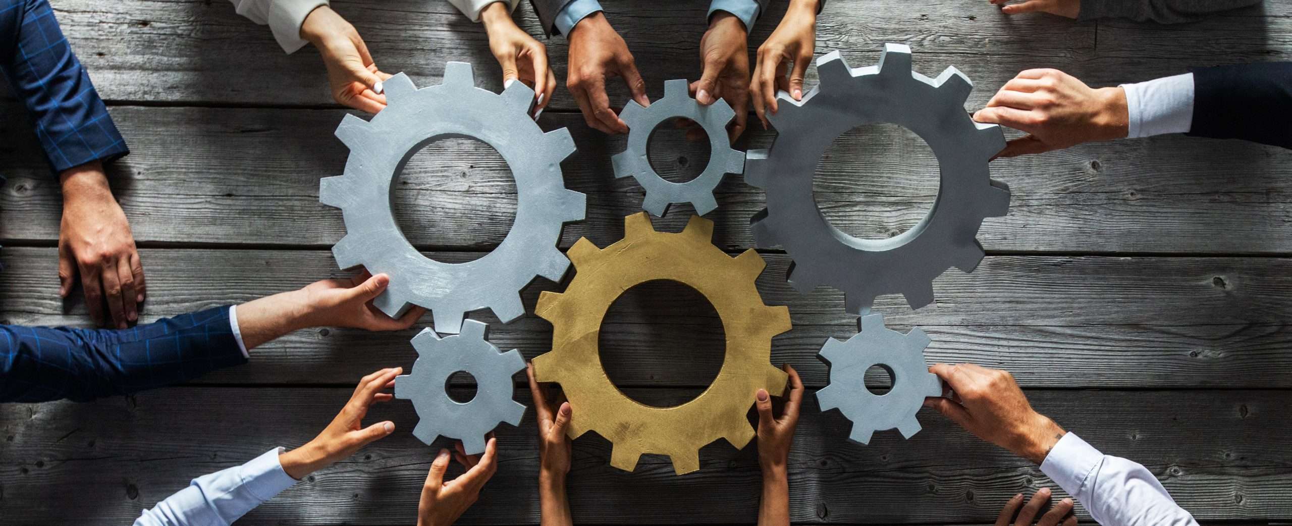 People with outstretched hands holding up cogs and gears